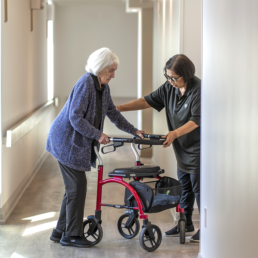 Caregiver assisting a resident with her walker in a bright hallway at Atrium Retirement Residence in Orillia