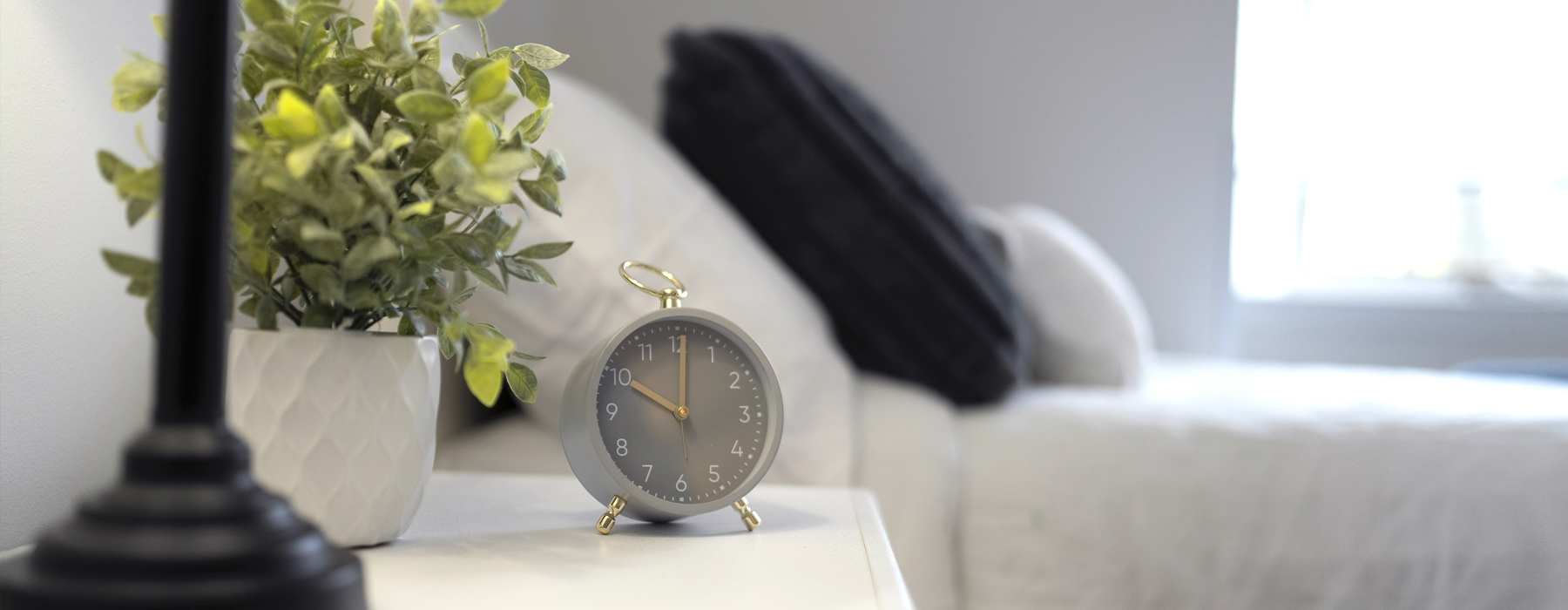 Close-up of a bedside table with clock and plant adding comfort to a bright private suite at Atrium Retirement Residence in Orillia