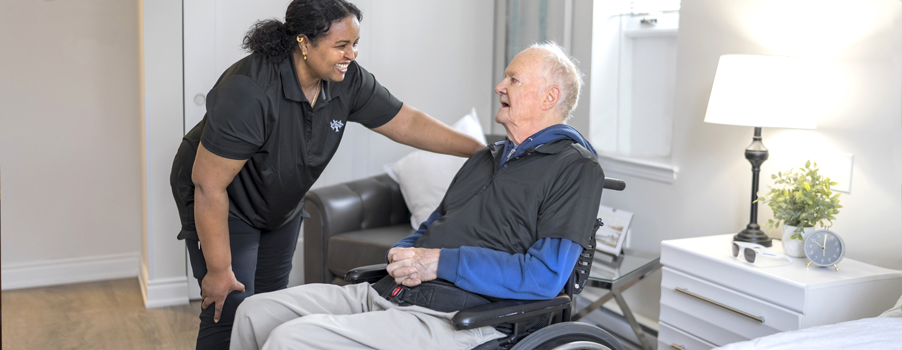 th_resident.jpg Caregiver sharing a warm smile with a resident in a wheelchair inside a bright, comfortable suite at Atrium Retirement Residence in Orillia