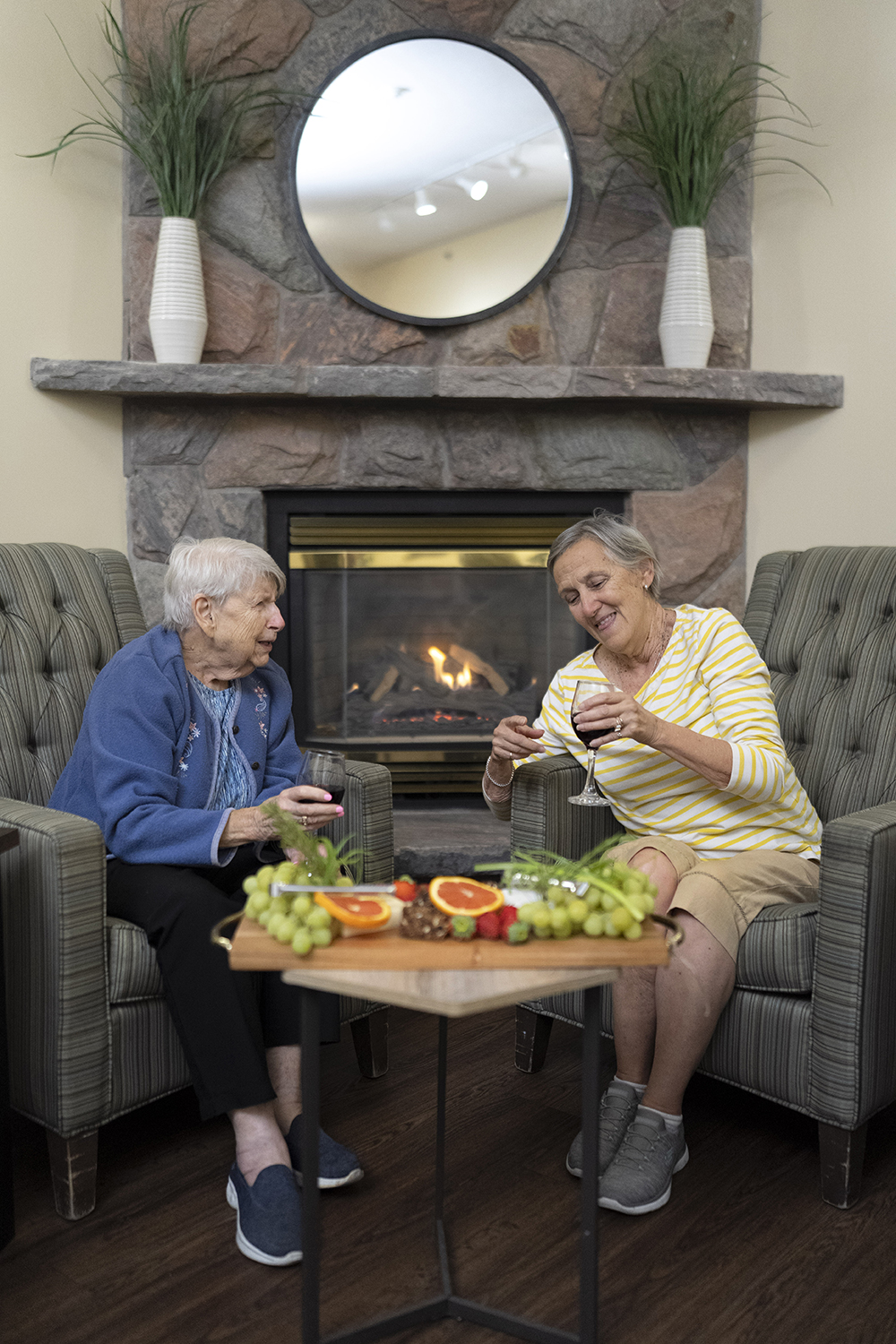 Two residents sharing wine and conversation by the fireplace lounge at Atrium Retirement Residence in Orillia