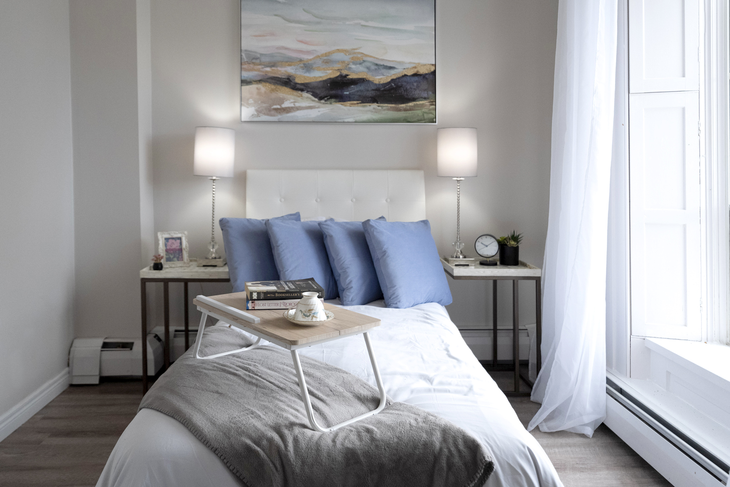 Model senior living suite bedroom at Atrium with blue pillows, bedside lamps, and a breakfast tray
