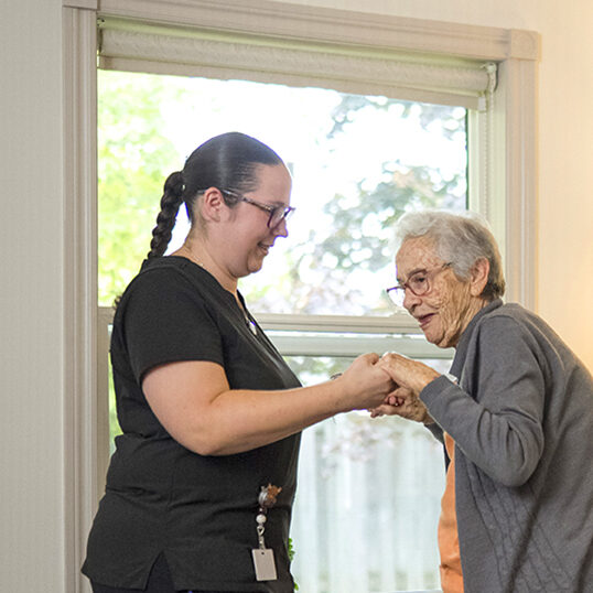 Nurse helping resident onto her feet in her room as part of Select Care services